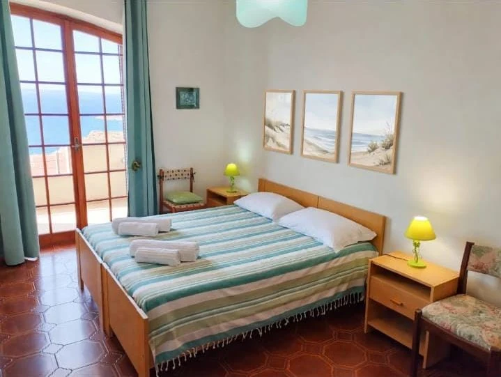 La camera con il copriletto a righe e la porta finestra sul mare