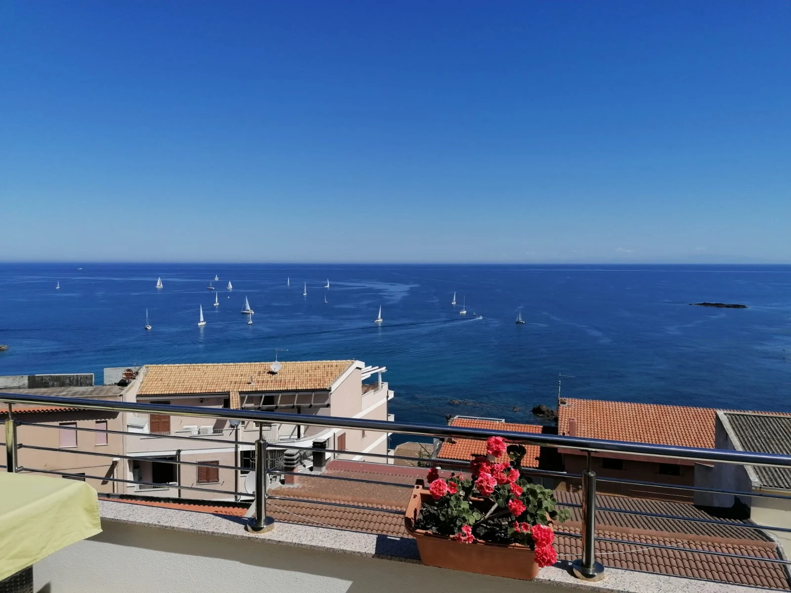 Il mare davanti al terrazzo punteggiato di barche a vela, con i gerani in primo piano